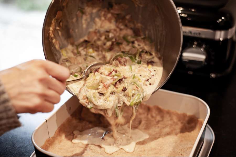 Rezept Foto Lauchzwiebelkuchen backen und genießen. Die angebratenen Zutaten werden zusammen mit der verquirlten Zutaten in die Springform gegeben.