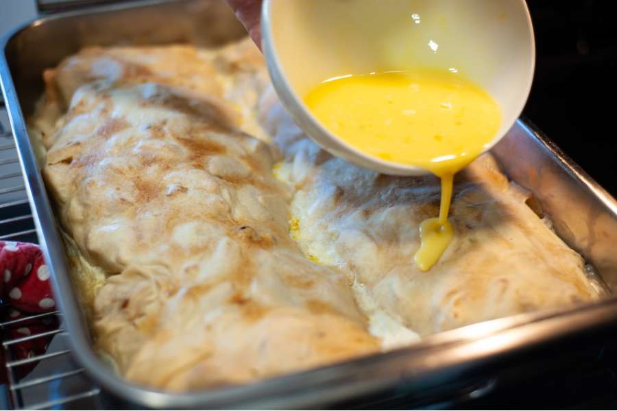 Rezept Foto Oberpfälzer Milchrahm Apfelstrudel. Mama Siglinde schüttet das gequirlte Ei langsam über den ersten Strudel.