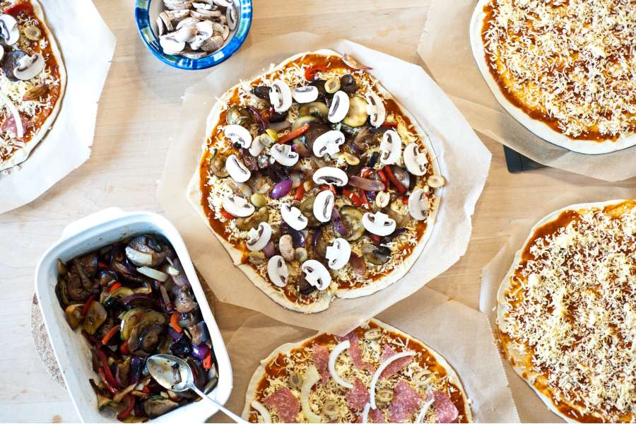 Rezept Foto Grillpizza und Ofenpizza Italien. Der Esstisch ist voll mit belegten Pizzas und vielen verschiedenen Zutaten.