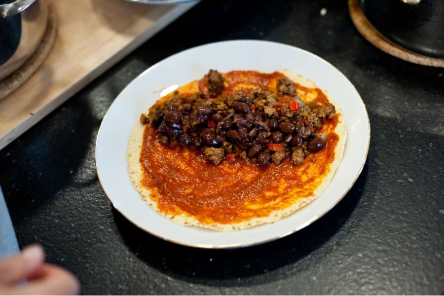 Rezept Foto Mexikansiche Enchillada. Auf die bestrichenen Maismehltortillas kommt nun eine Reihe gegrilltes Hackfleisch, schwarze Bohnen und etwas Käse.