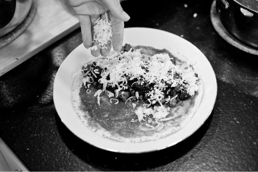 Rezept Foto Mexikansiche Enchillada. Katharina streut den Käse langsam über die Tortillas.