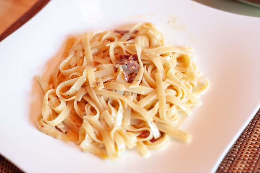 Rezept Foto Spaghetti Carbonara. Die Nudeln werden auf einem großen Teller angerichtet und mit Pecorino verfeinert.
