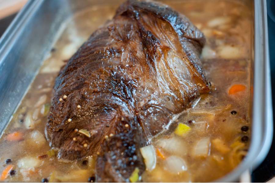 Rezept Foto Sauerbraten mit Serviettenknödel. Der Braten wird gerade mit Gemüsebrühe aufgegossen bis er mindestens ein viertel der Höhe bedeckt wird. Der Braten wird gleich in der Röhre schmoren.